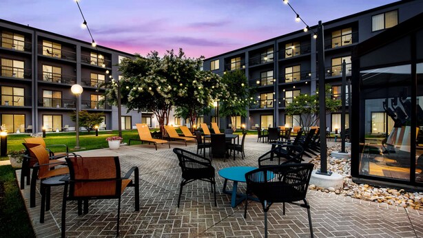 A courtyard with outdoor seating, a large building with multiple balconies, and string lights. - Sonesta Select Philadelphia Airport (Philadelphia)