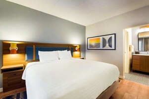 Habitación de hotel con una cama grande, cabecera de madera, mesitas de noche, una lámpara de pared y un cuadro enmarcado.