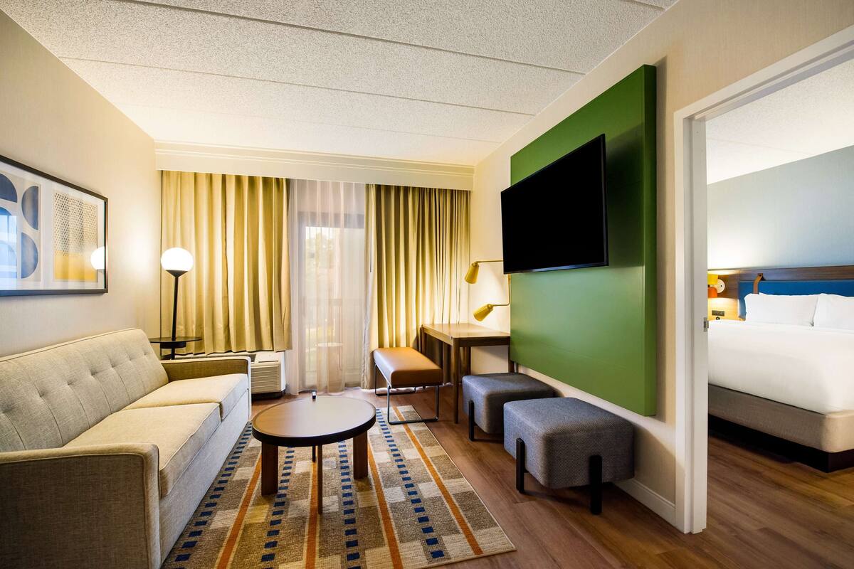 A hotel room with a sofa, a round table, a bench, a TV, and a bed.