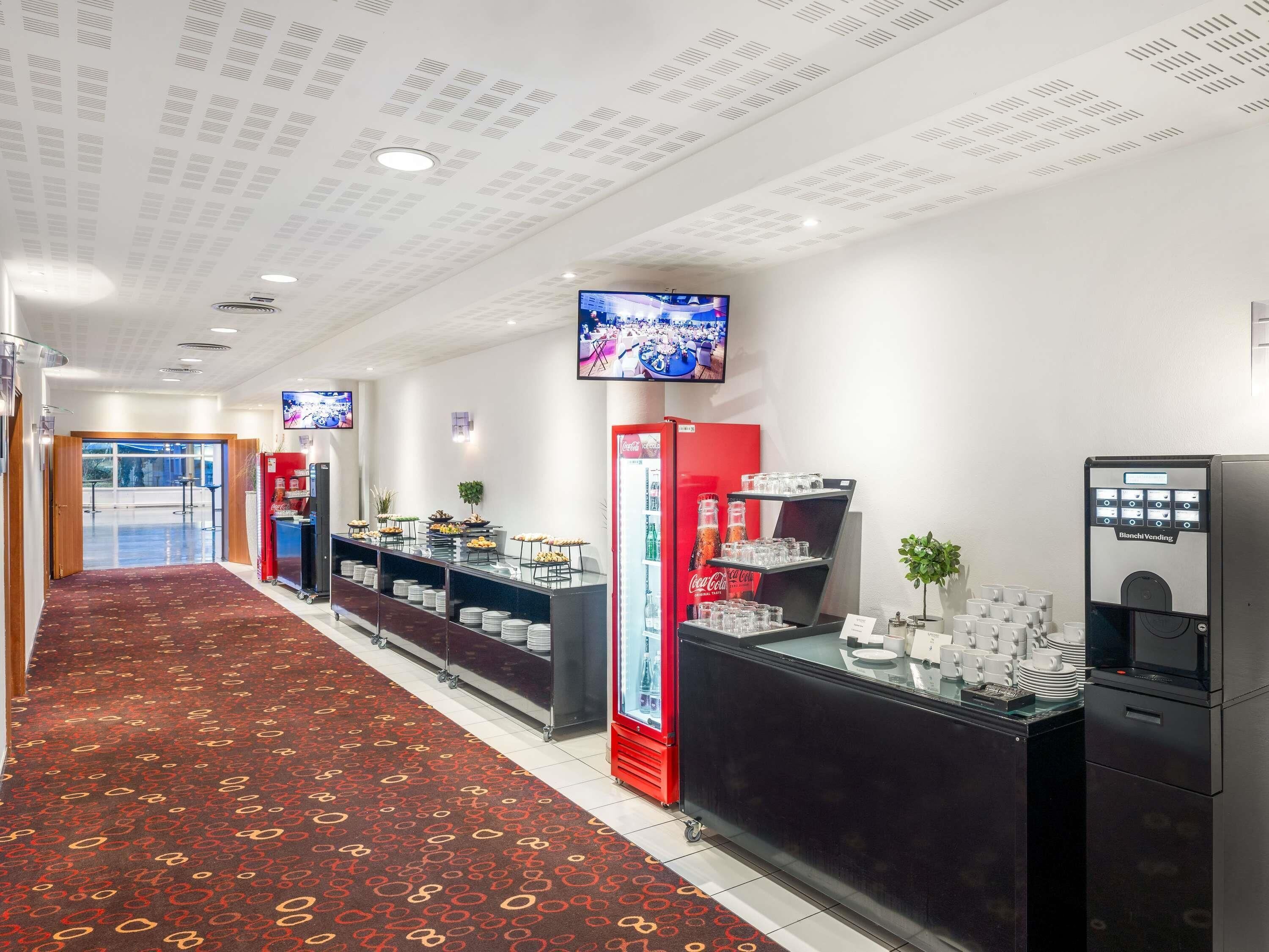 A hotel lobby with a red carpet, a Coca-Cola refrigerator, a vending machine, and a television screen.