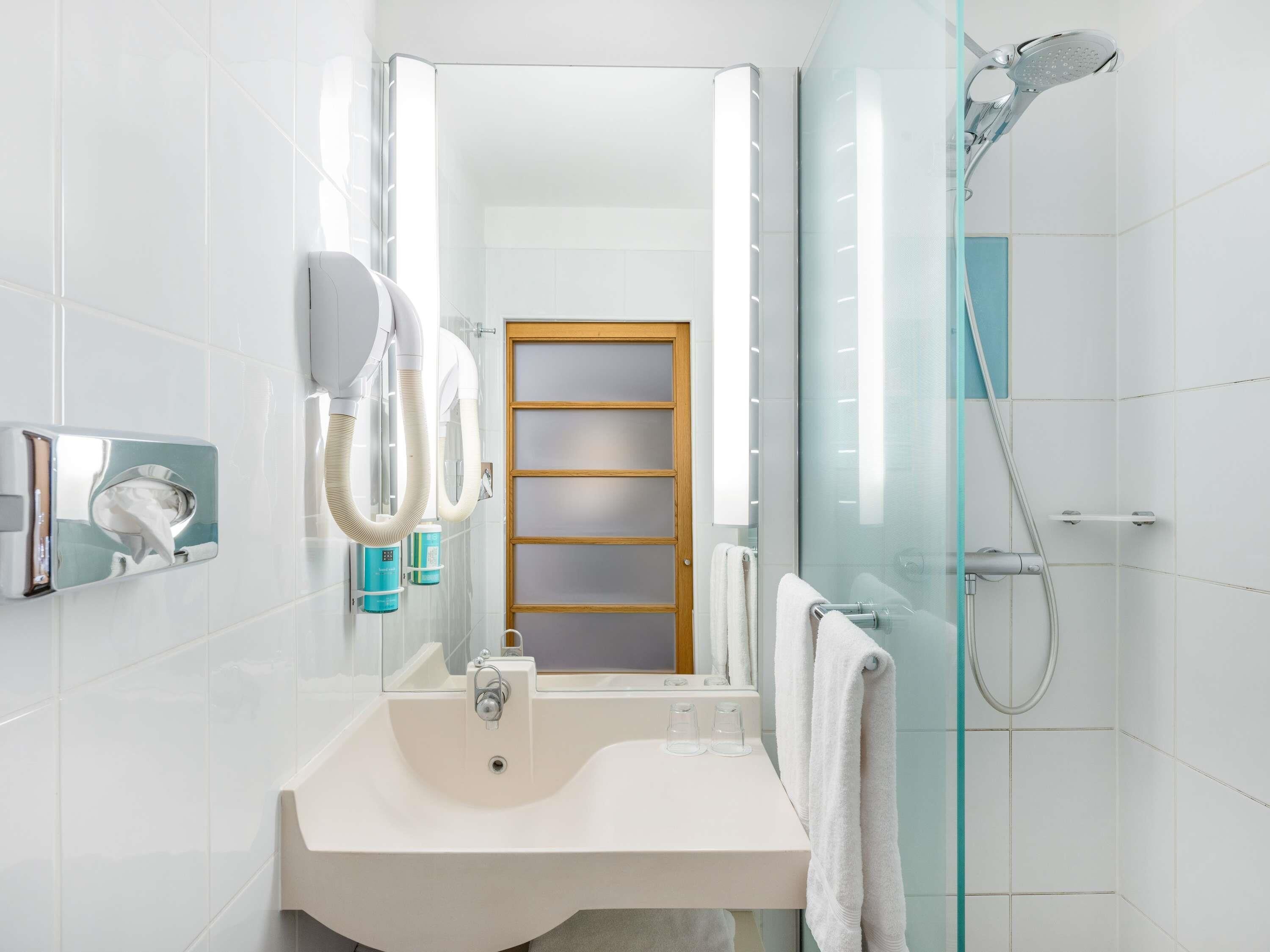 Ein modernes Badezimmer mit Waschbecken, Spiegel, Handtuchhalter und einer Duschkabine.