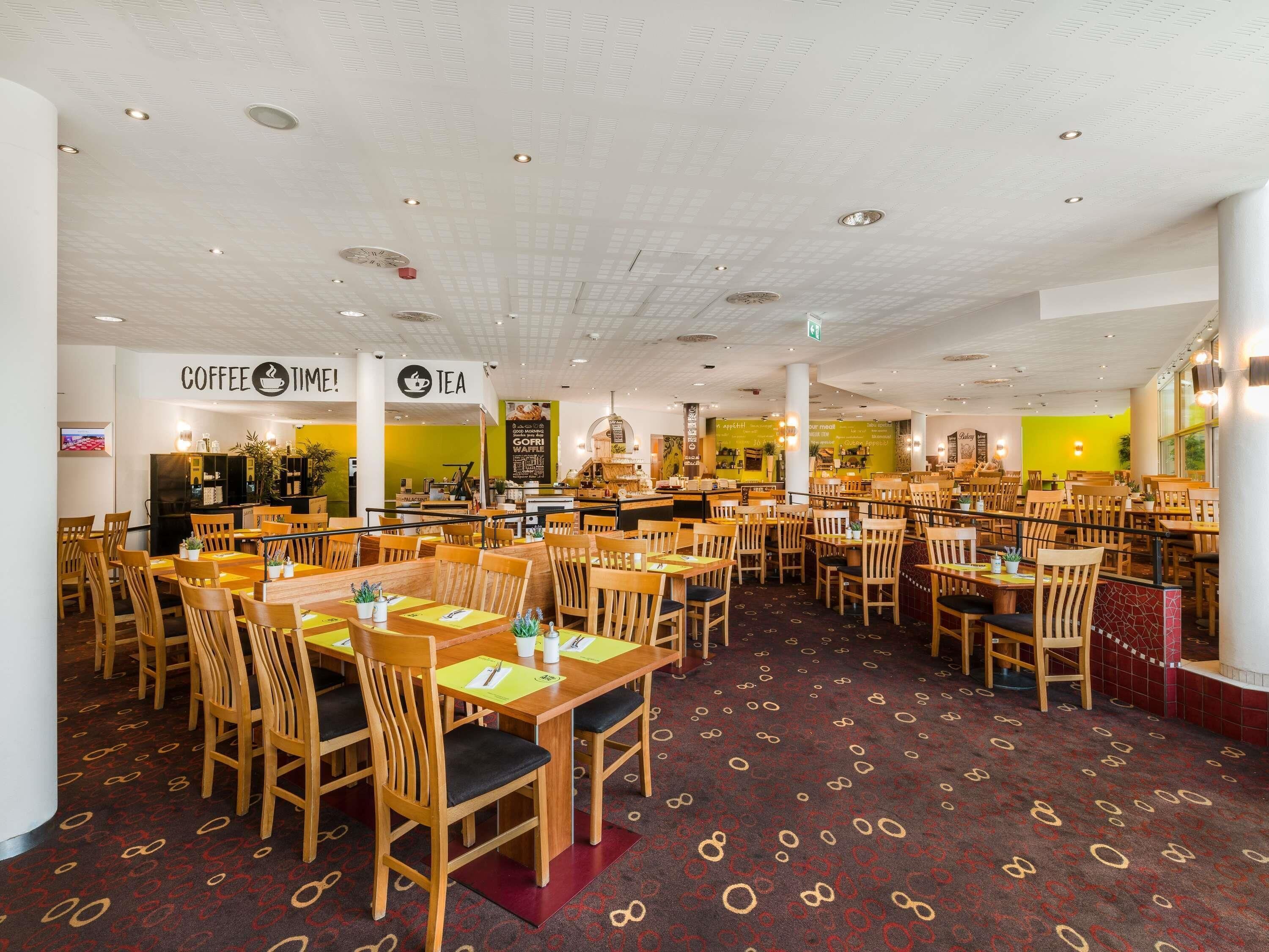 A spacious cafe with wooden tables and chairs, a coffee and tea sign, and a menu board.