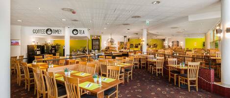 A spacious cafe with wooden tables and chairs, a coffee and tea sign, and a menu board.