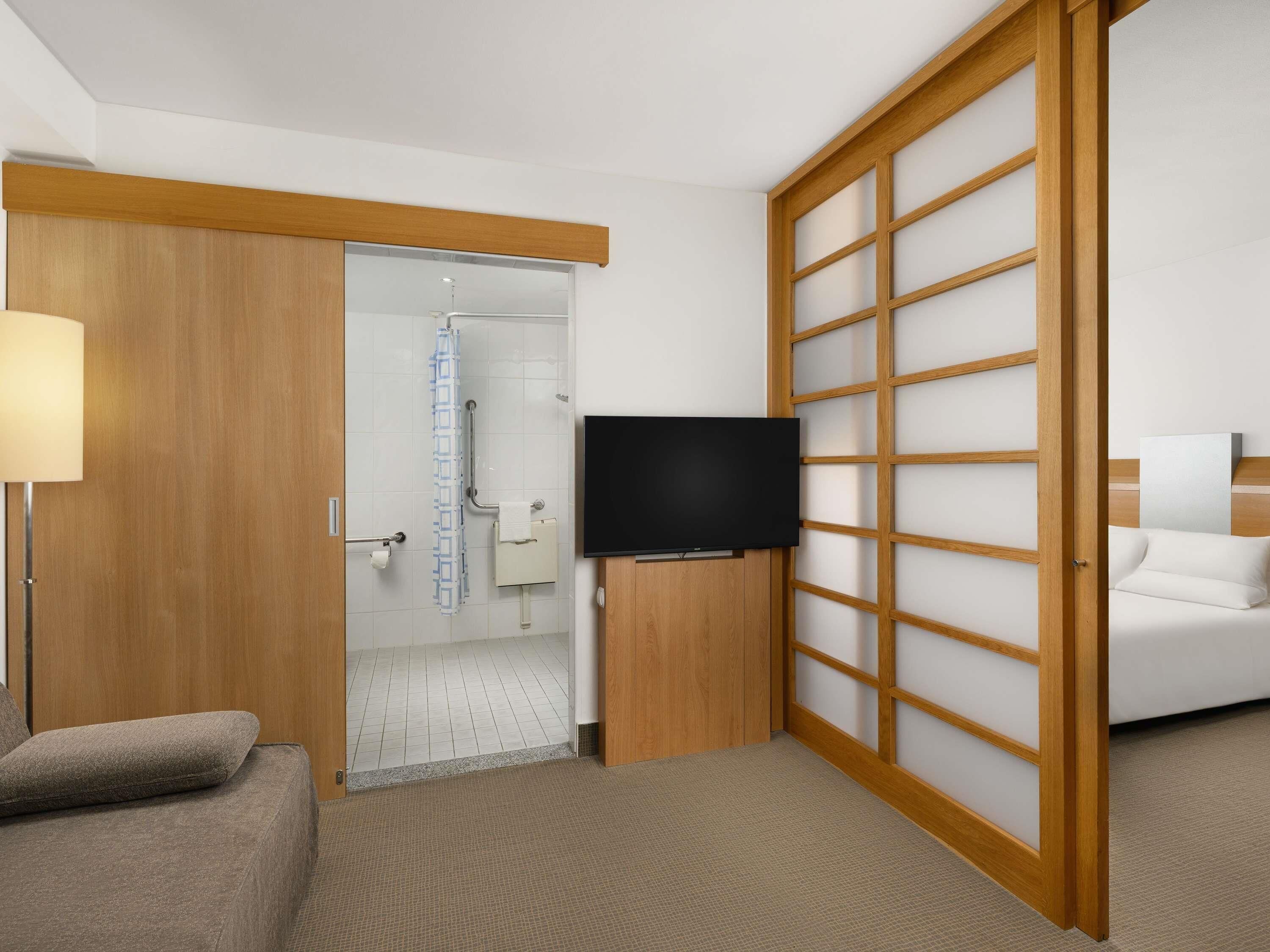 A hotel room with a sliding door, a television, a sofa, and a bathroom visible through the door.