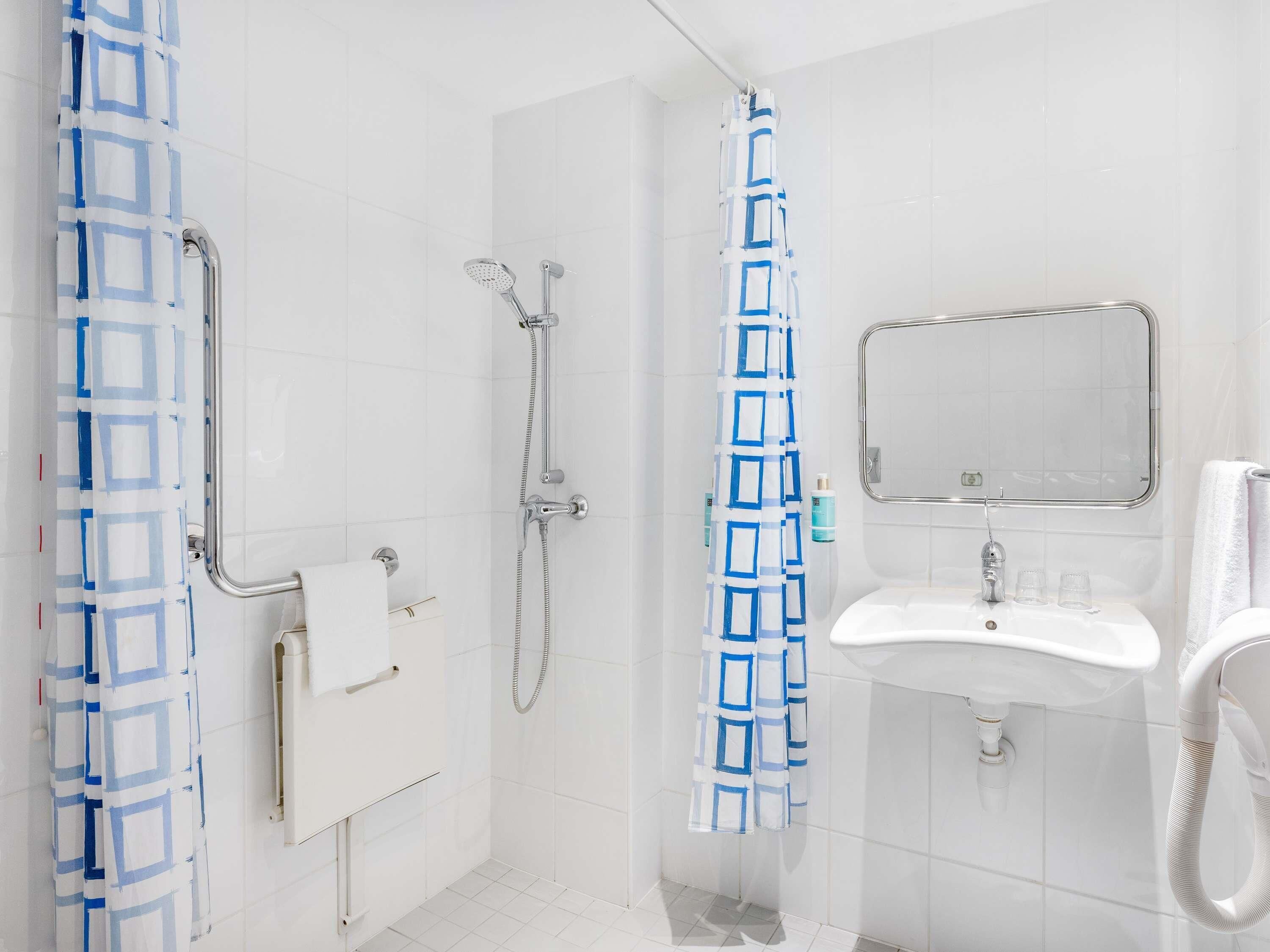 A bathroom with a shower, a sink, a mirror, and a towel rack.