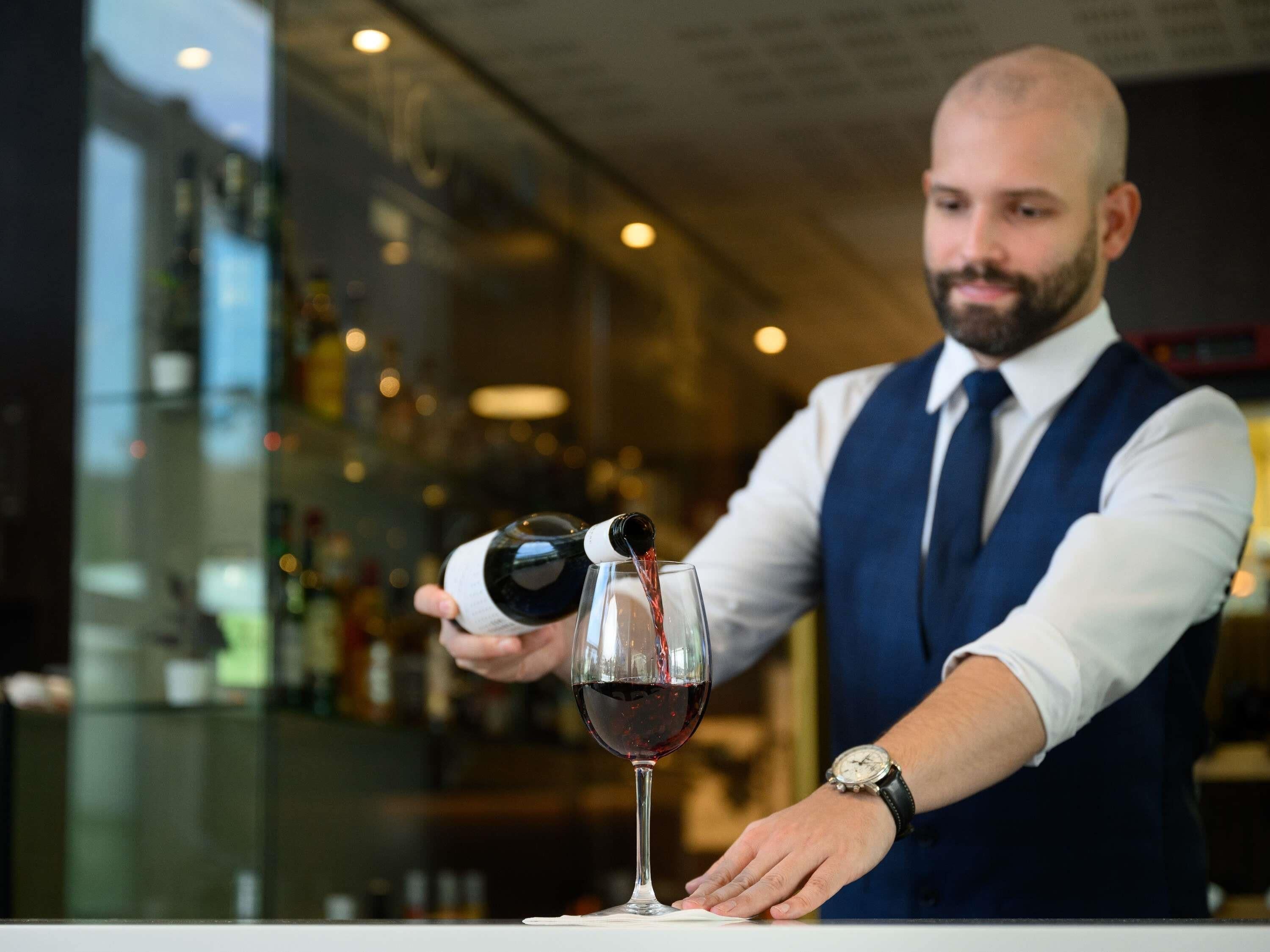 A bartender pouring wine into a glass.