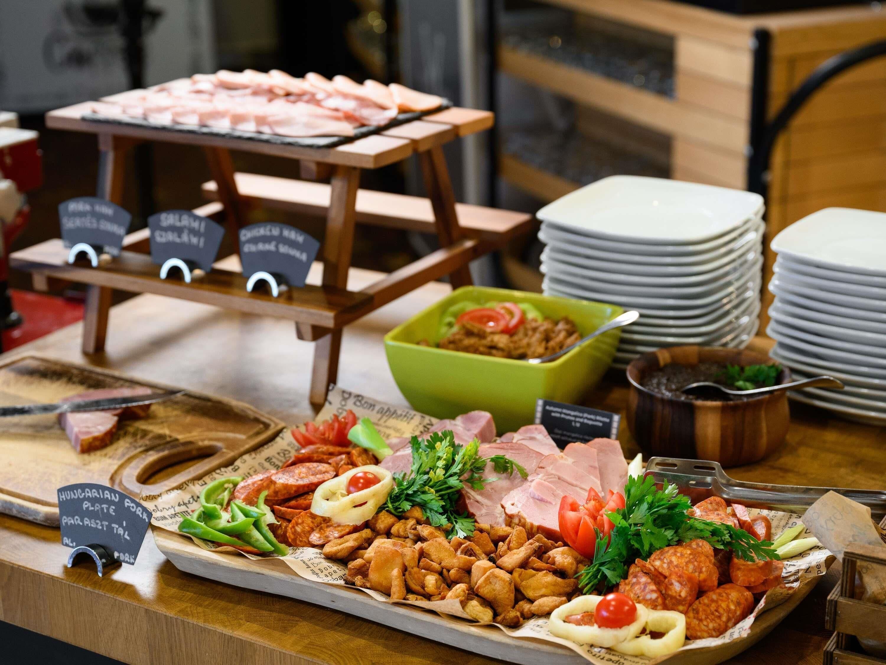 A buffet with various meats, vegetables, and a green bowl of salad.