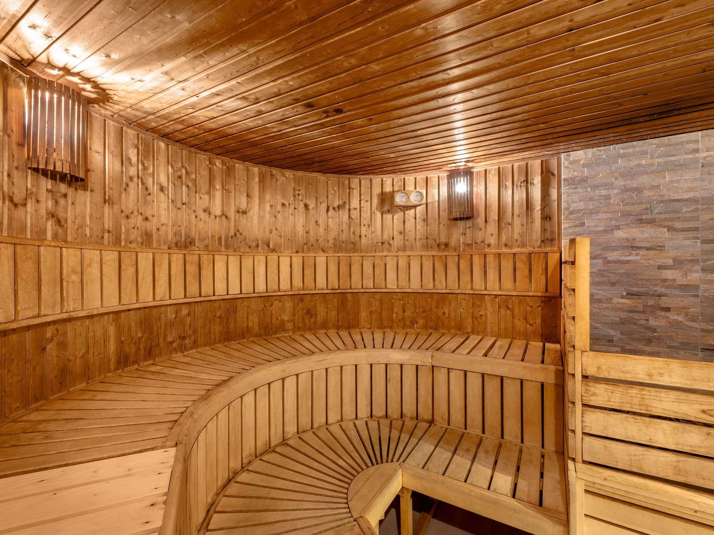 Una sauna de madera con un banco curvo y pared de piedra.