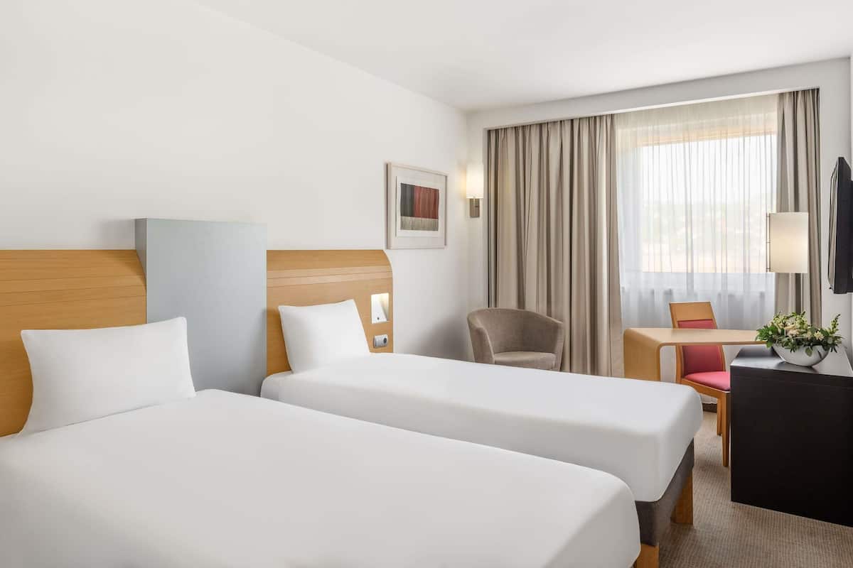A hotel room with two beds, a desk, a chair, a TV, and a window with curtains.