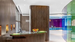 A reception desk with a glass top, a bowl of fruit, and a pool area in the background.