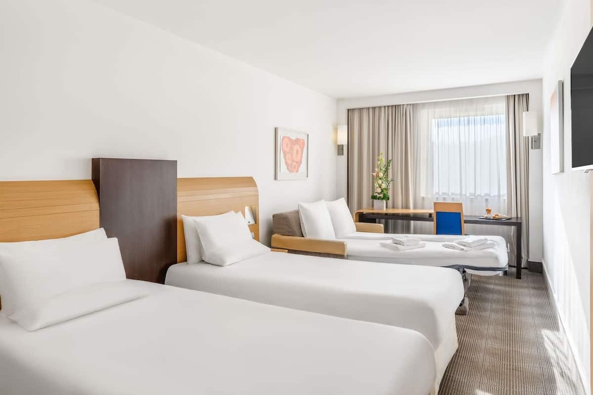 A hotel room with two beds, a desk, a chair, a TV, and a window with curtains.