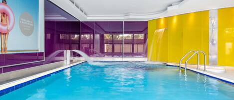 Una piscina interior con agua azul cristalina, pared amarilla y una cascada.