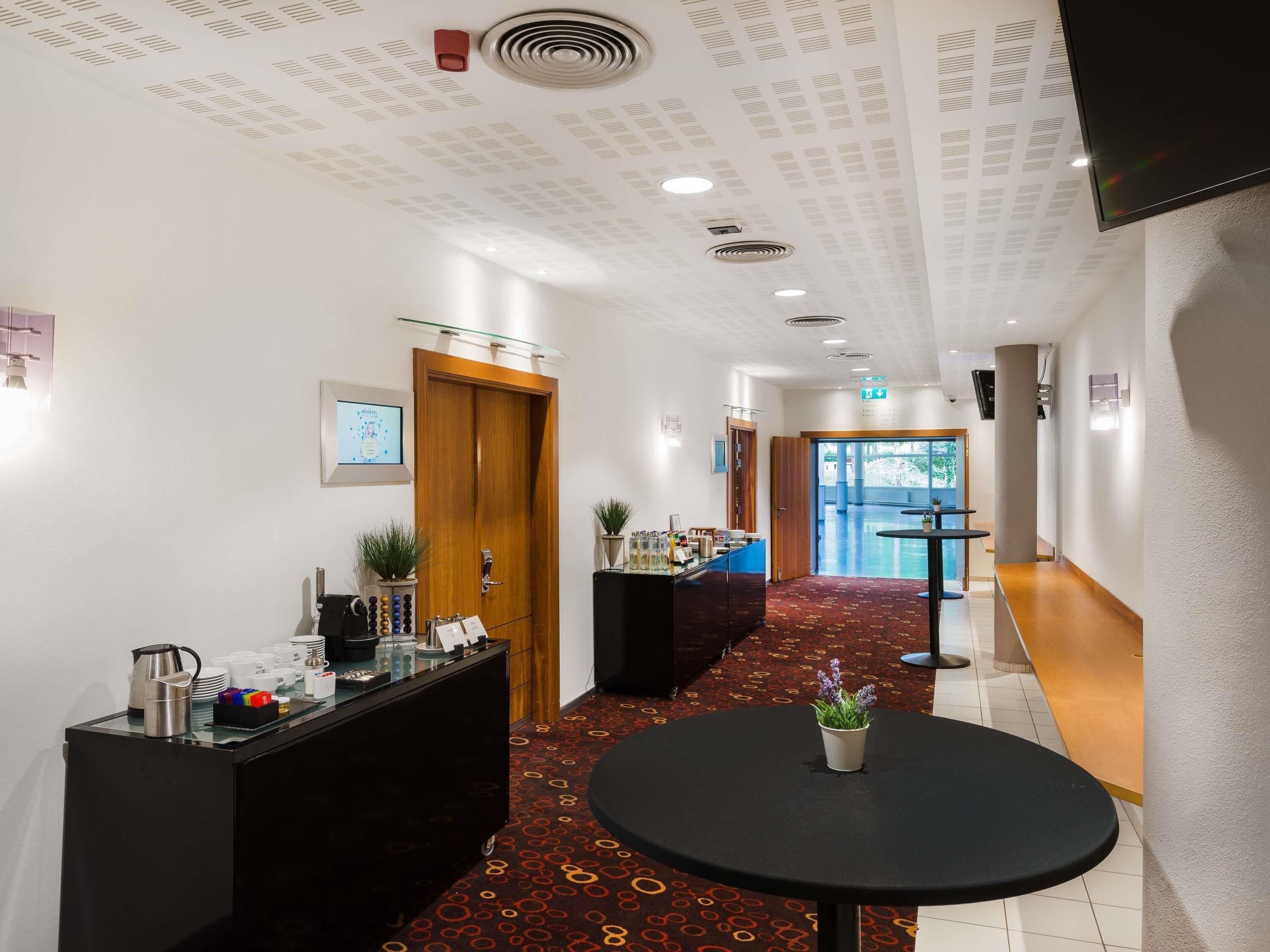 Rebedor d'hotel amb taulell de recepció, racó de cafè, taula petita amb una planta i una catifes amb disseny.