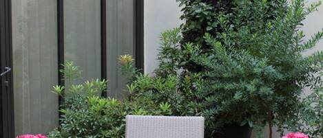 A round wicker table with a tray, two potted pink hydrangeas, a chair, and a large potted plant.