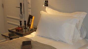 A neatly made bed with white linens, a bedside table with a lamp, a framed picture, and a book.