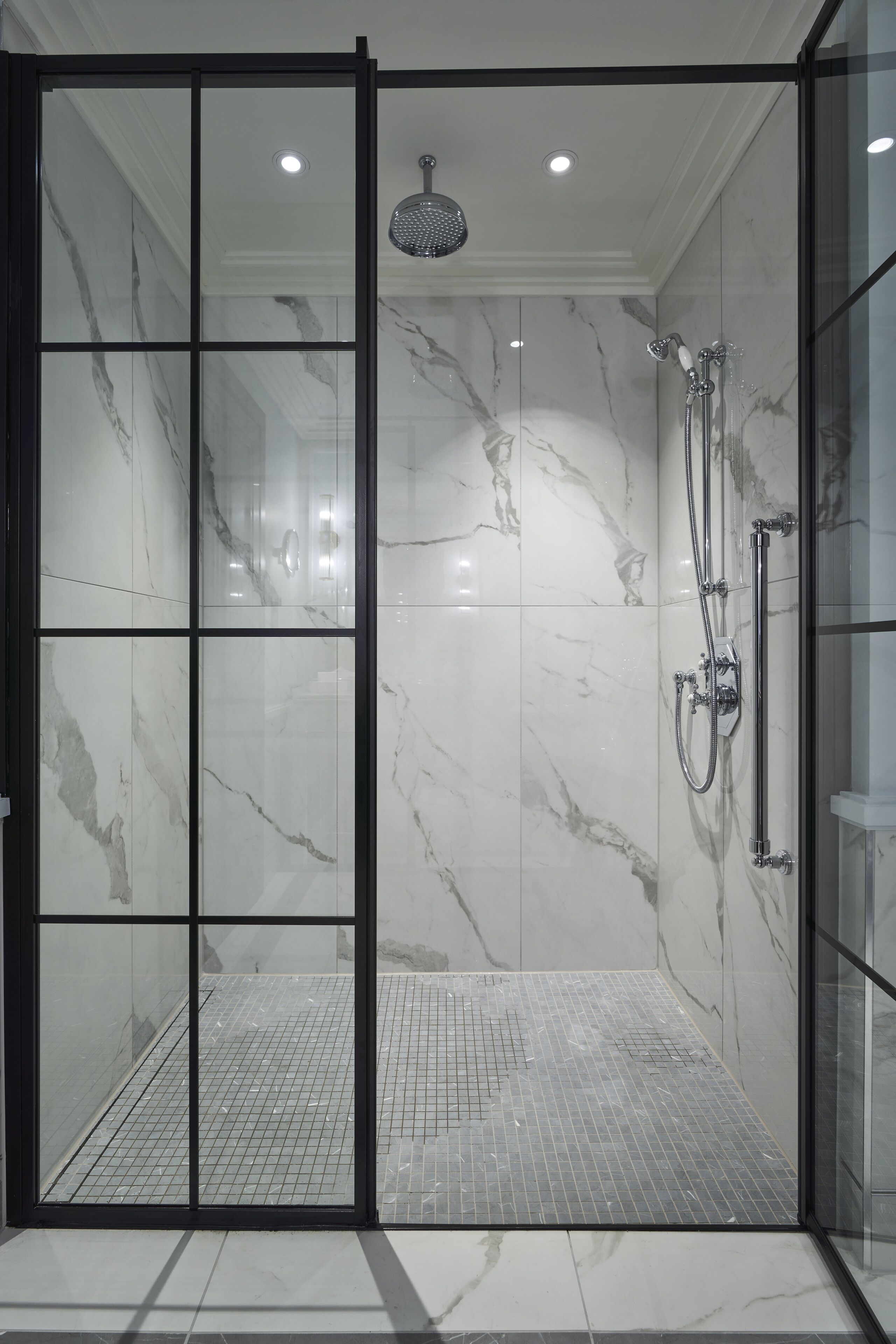 Een moderne douche met glazen wand, marmeren wanden en een betegelde vloer.