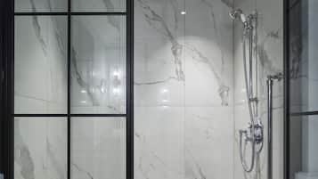 A modern shower area with a glass partition, marble walls, and a tiled floor.