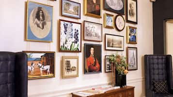 A room with a wall adorned with framed artworks, a wooden console table with papers, and two upholstered armchairs.