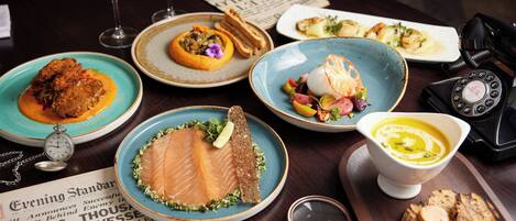 A table with various dishes, a newspaper, a wine glass, a pocket watch, and a rotary phone.