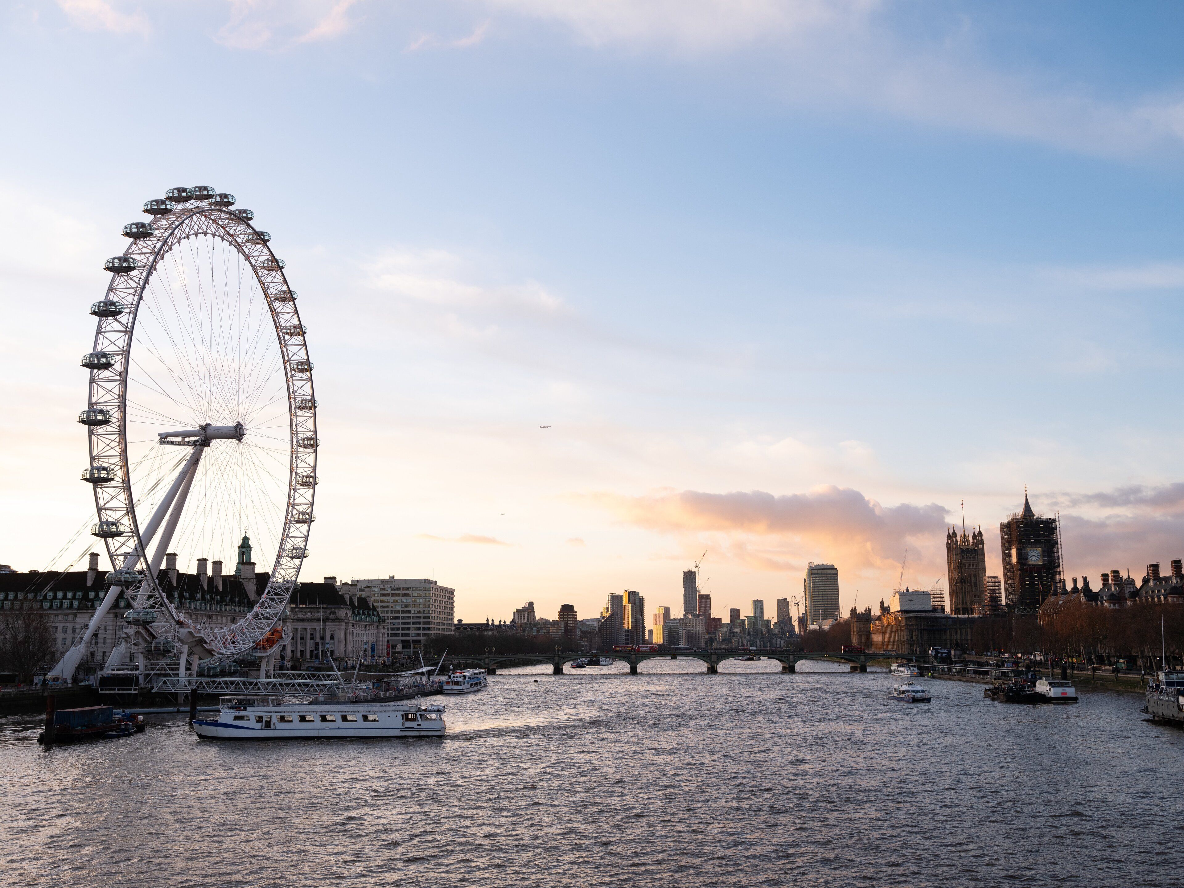 A river with boats and a large Ferris wheel in the background.