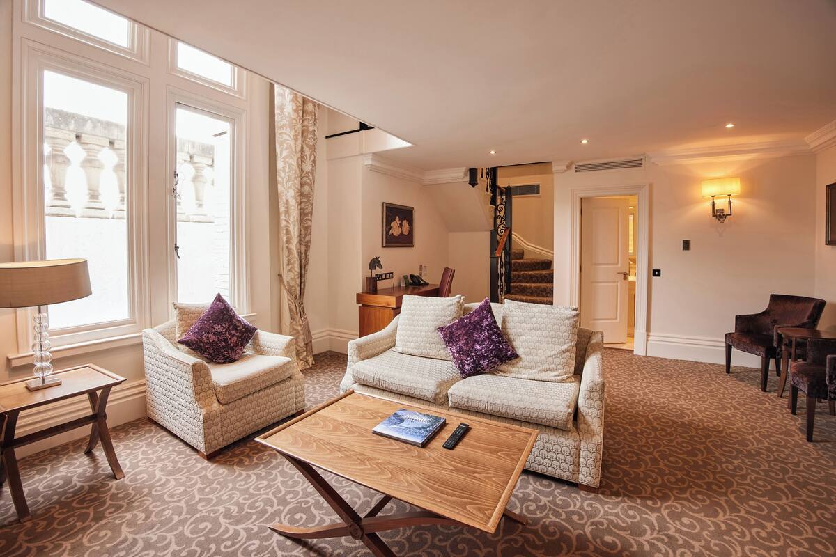 A spacious living room with a sofa set, a coffee table, and a staircase leading to an upper floor.