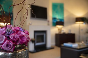 Ein Wohnzimmer mit Kamin, einem an der Wand befestigten Fernseher und einer Tischvase mit Blumen.