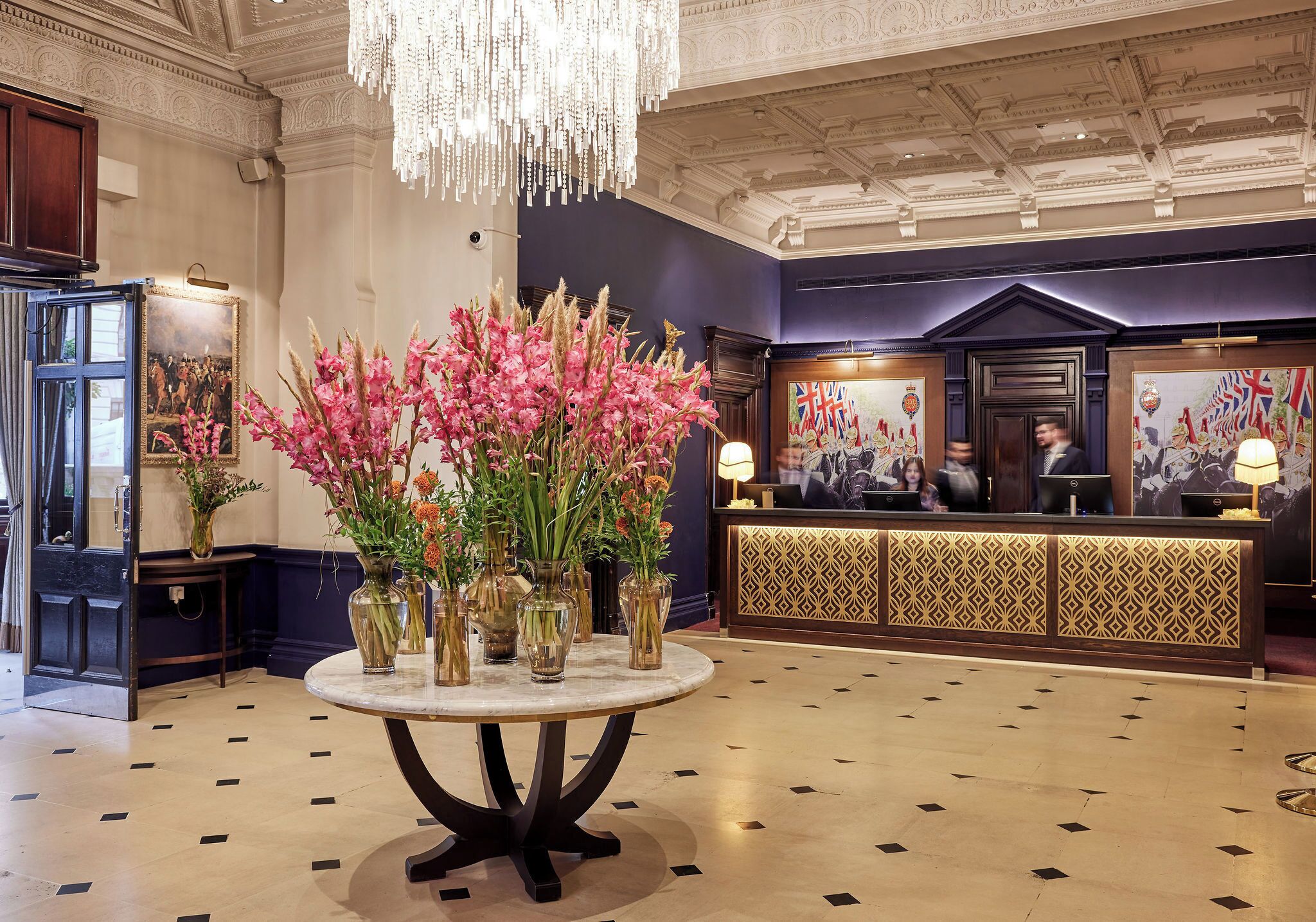 A lobby with a reception desk, a chandelier, and a table with vases of flowers.