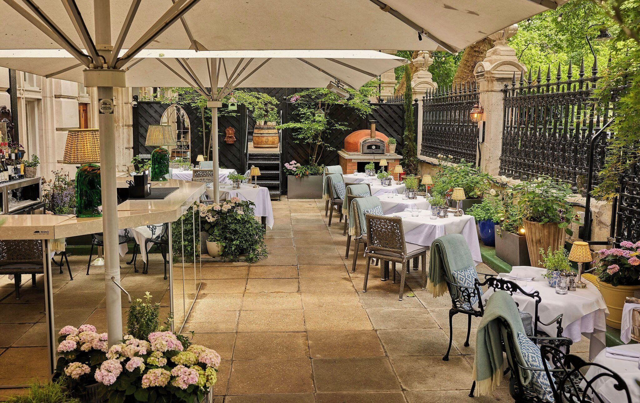 An outdoor dining area with tables and chairs, a pizza oven, and potted plants.