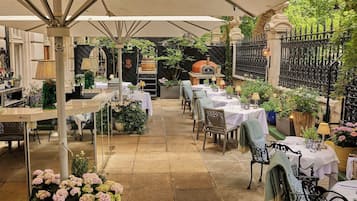 An outdoor dining area with tables and chairs, a pizza oven, and potted plants.