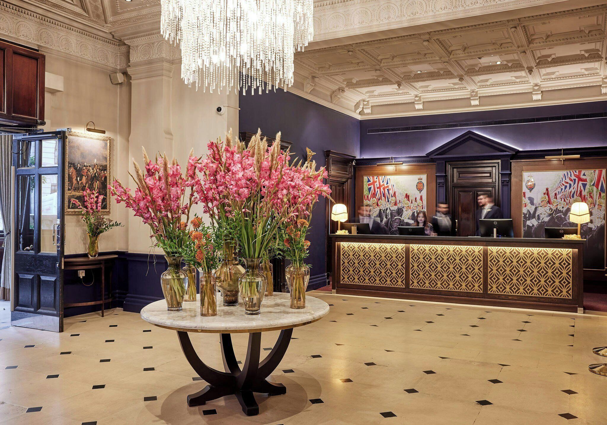 A lobby with a reception desk, a chandelier, and a table with vases of flowers.