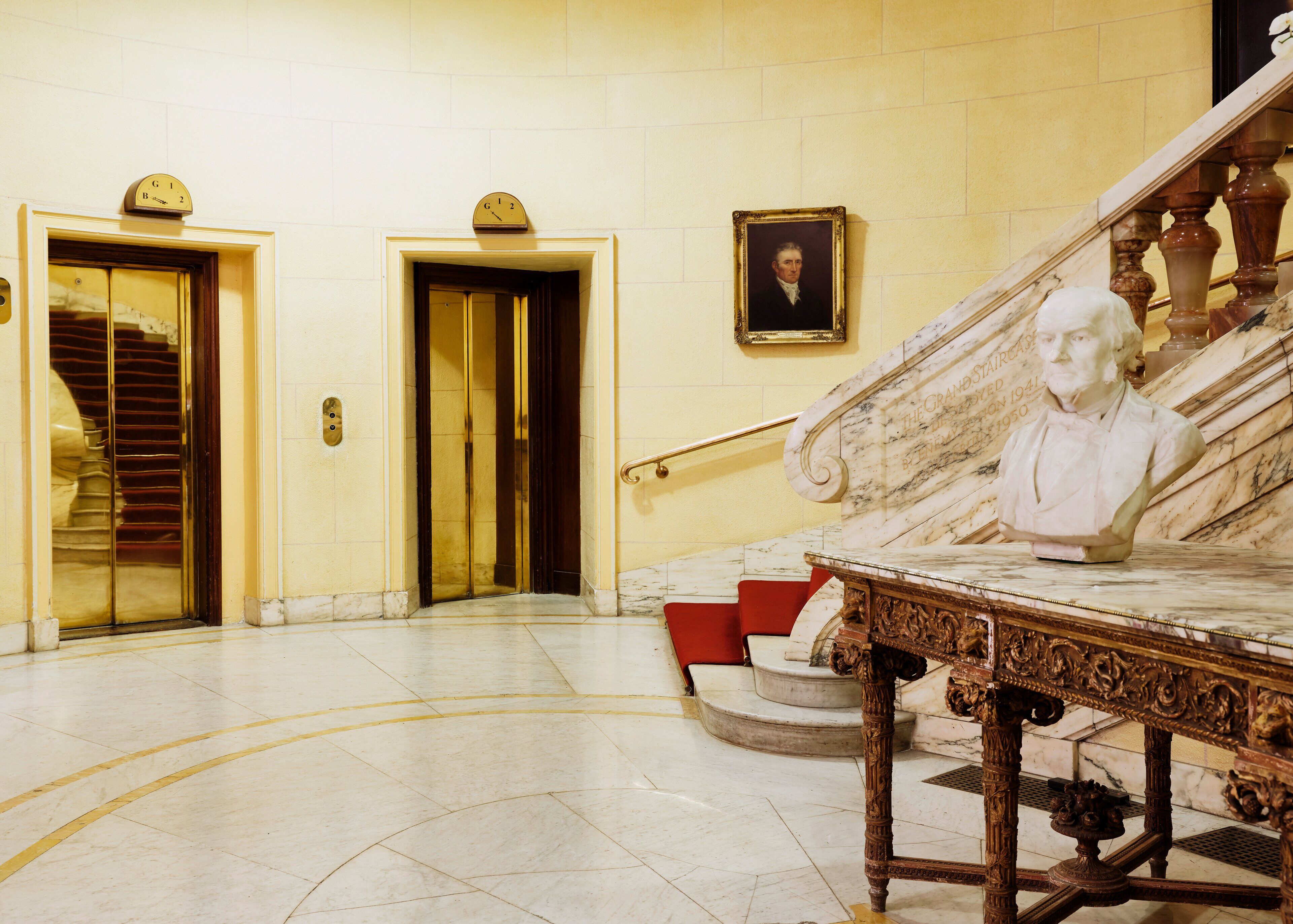 Een statige trap met een marmeren balustrade, een borstbeeld en een lijstwerkportret aan de muur.