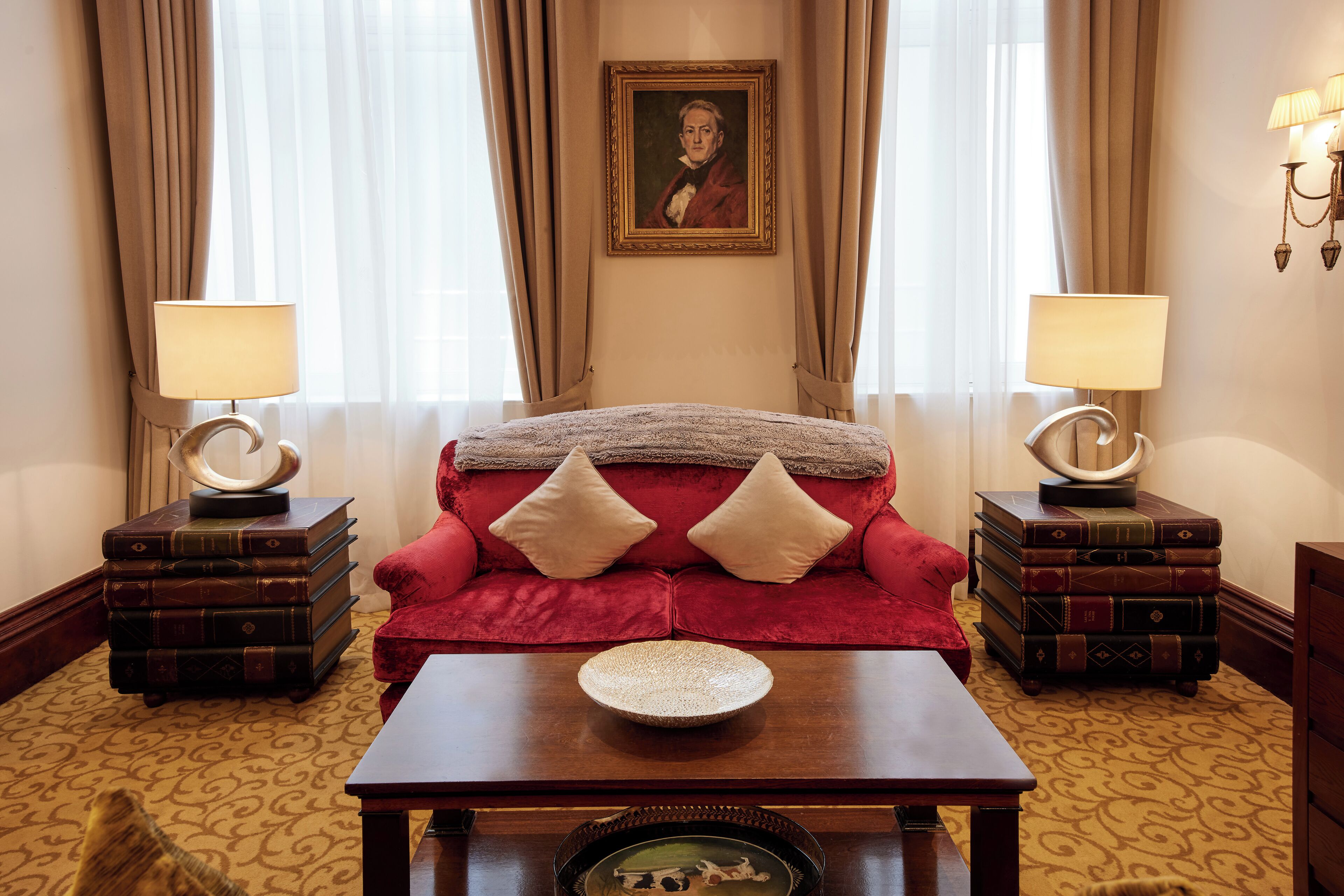 A red sofa with two pillows, a wooden coffee table, and two bedside tables with lamps.