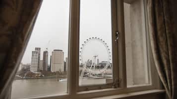 A view of a cityscape through a window with curtains, including a prominent Ferris wheel and tall buildings.