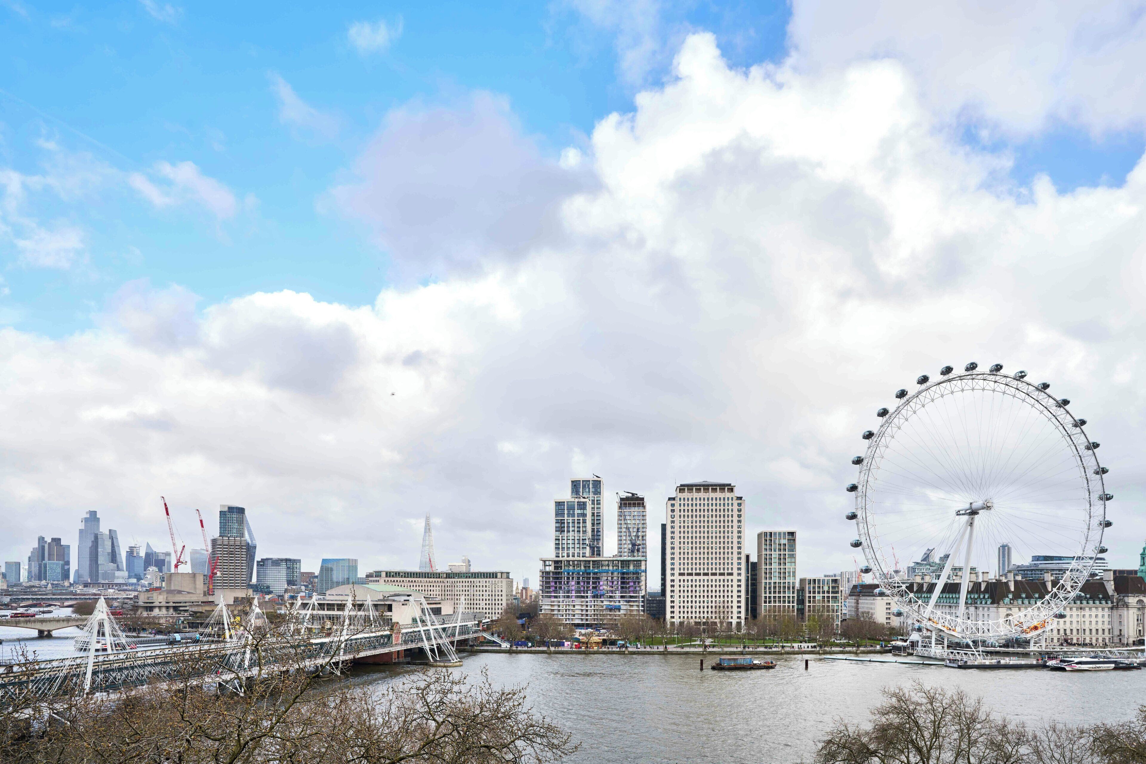 A cityscape with a prominent Ferris wheel, modern buildings, and a bridge over a river.