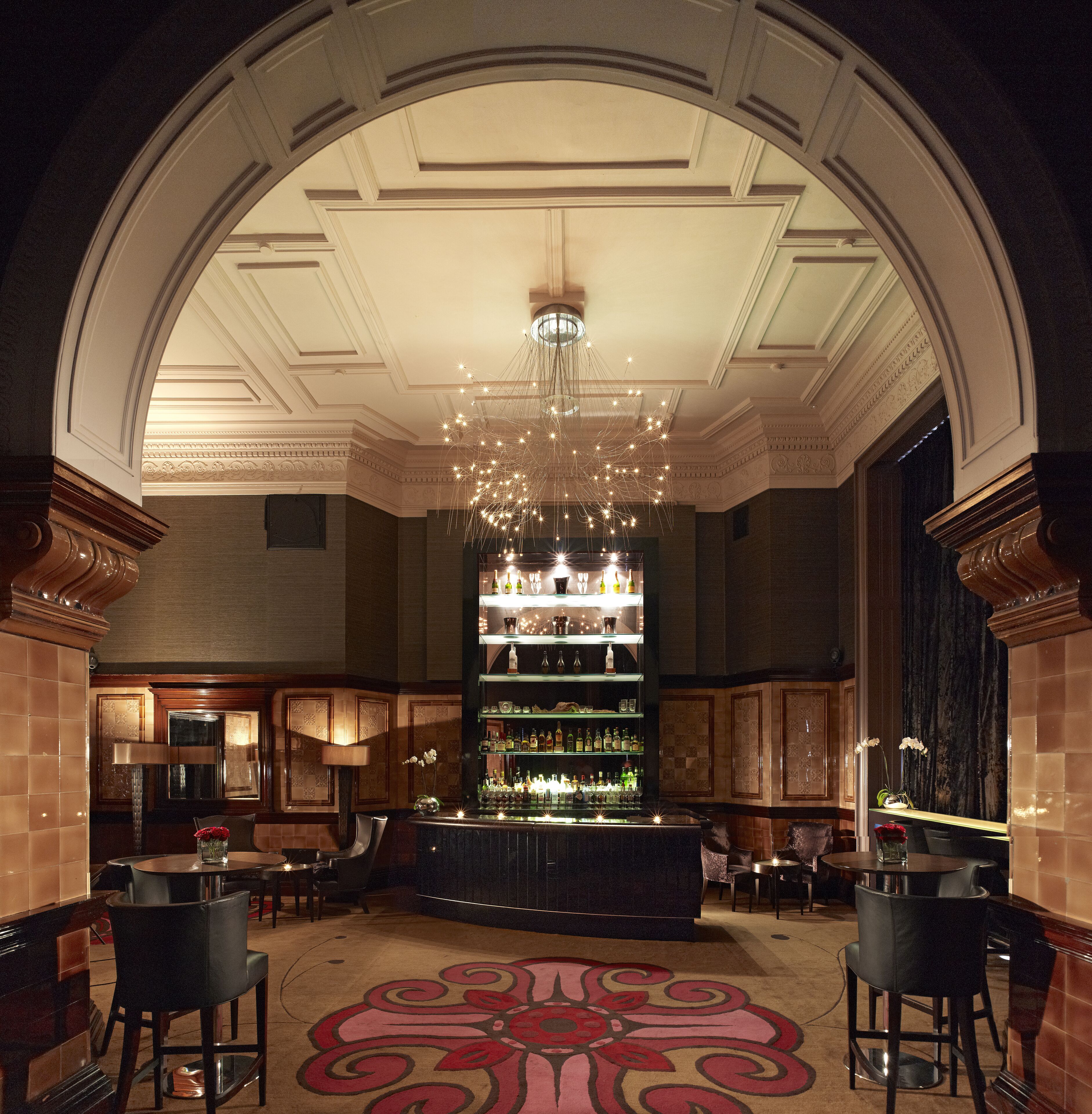 A bar area with a chandelier, bar shelves, and seating.
