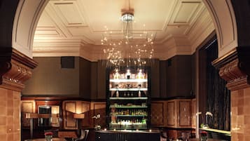 A bar area with a chandelier, bar shelves, and seating.