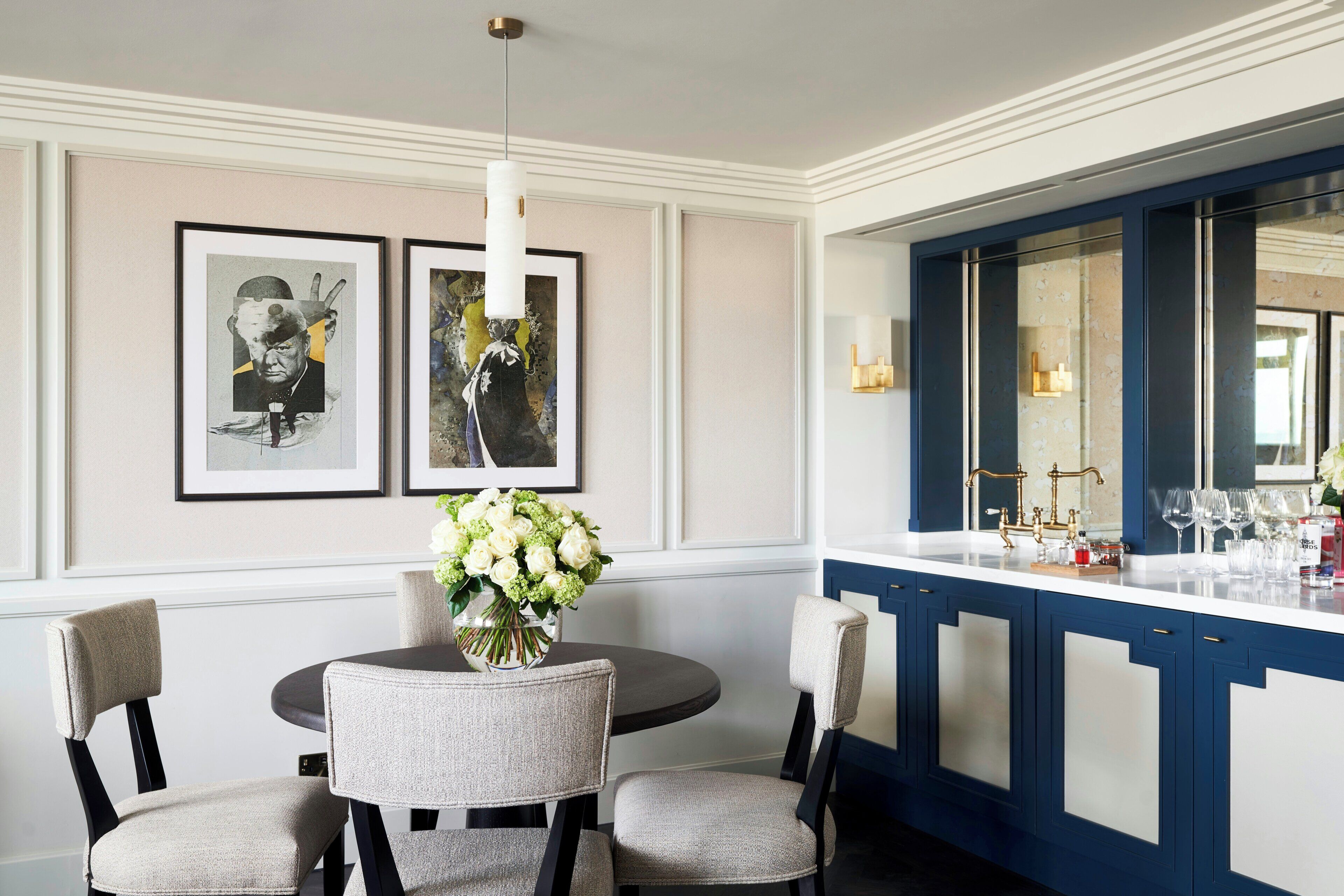 A dining area with a round table, four chairs, a vase of flowers, and two framed artworks on the wall.