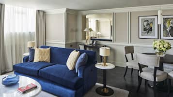 A modern living room with a blue sofa, a round coffee table, a dining table with chairs, and a large mirror.