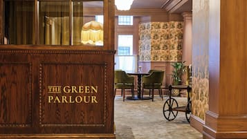 Un espace d’accueil avec un bureau en bois portant l’inscription « The Green Parlour », des chaises vertes, une petite table et une lampe décorative.