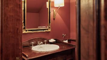 A bathroom with a wooden vanity, a white sink, a gold-framed mirror, and a wall-mounted lamp.