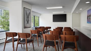 Une salle de conférence avec des rangées de chaises en bois, une grande fenêtre et un téléviseur à écran plat fixé au mur.