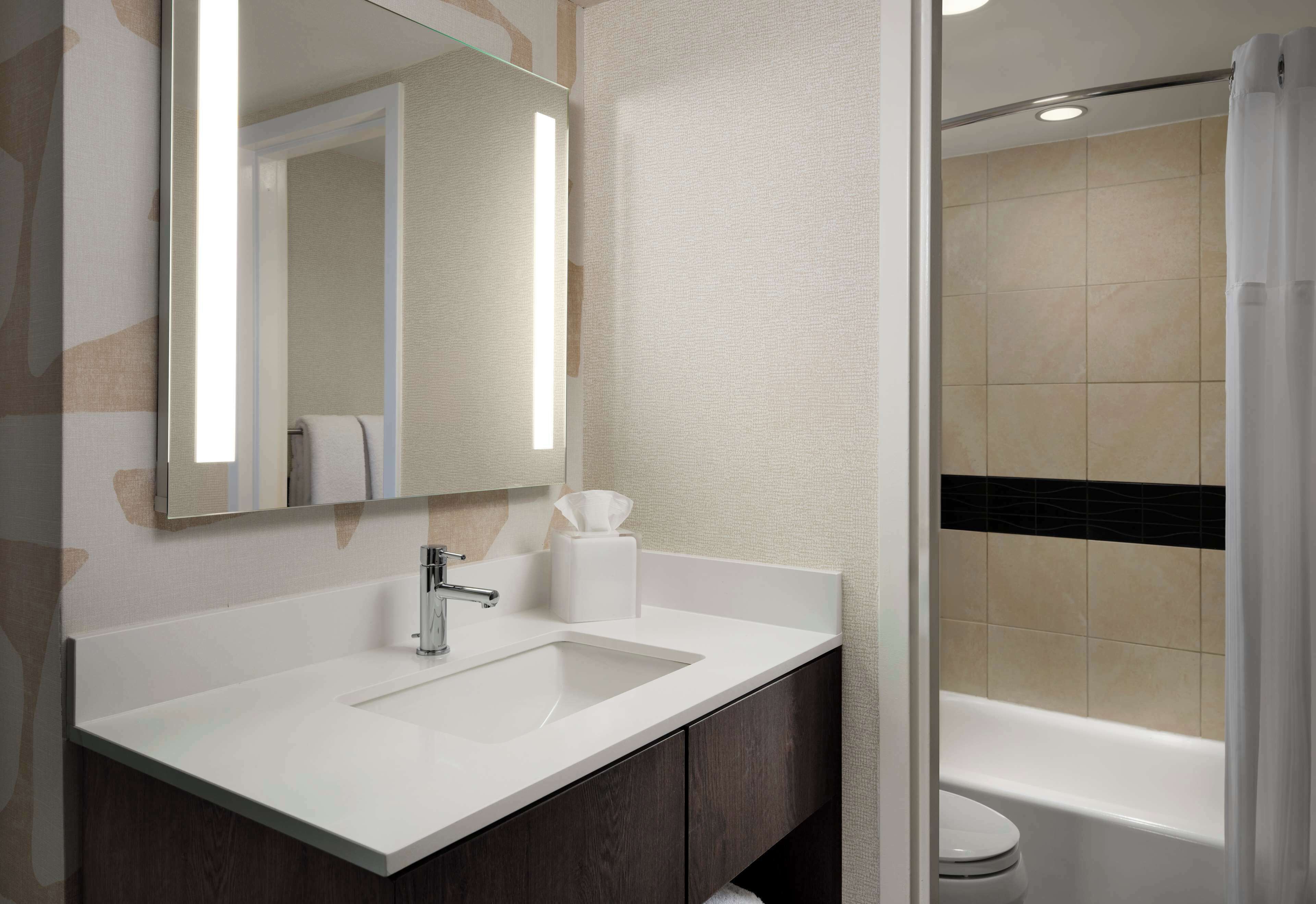 A bathroom with a white sink, dark wooden cabinets, a mirror, and a shower area.