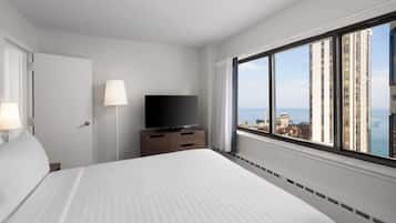 A hotel room with a large bed, a TV on a wooden dresser, and a view of the city through a large window.