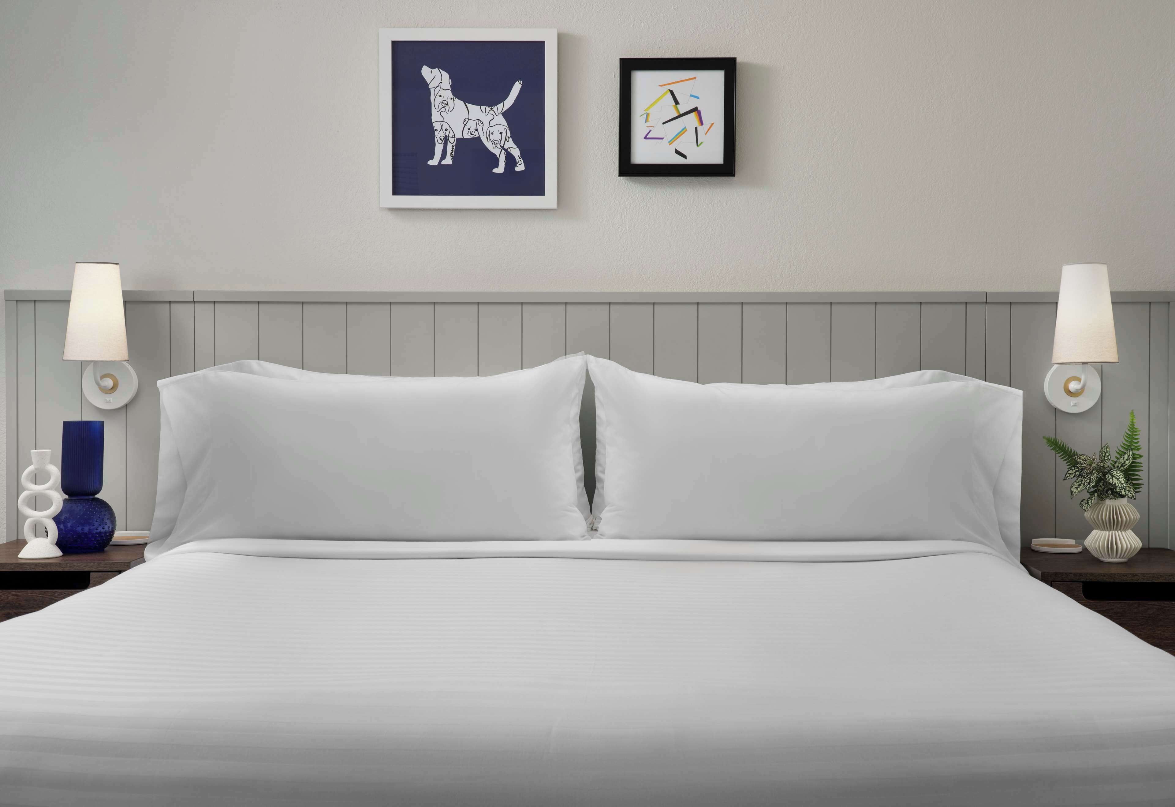 Un lit bien fait, avec du linge de lit blanc, une tête de lit grise et deux lampes fixées au mur, une de chaque côté.
