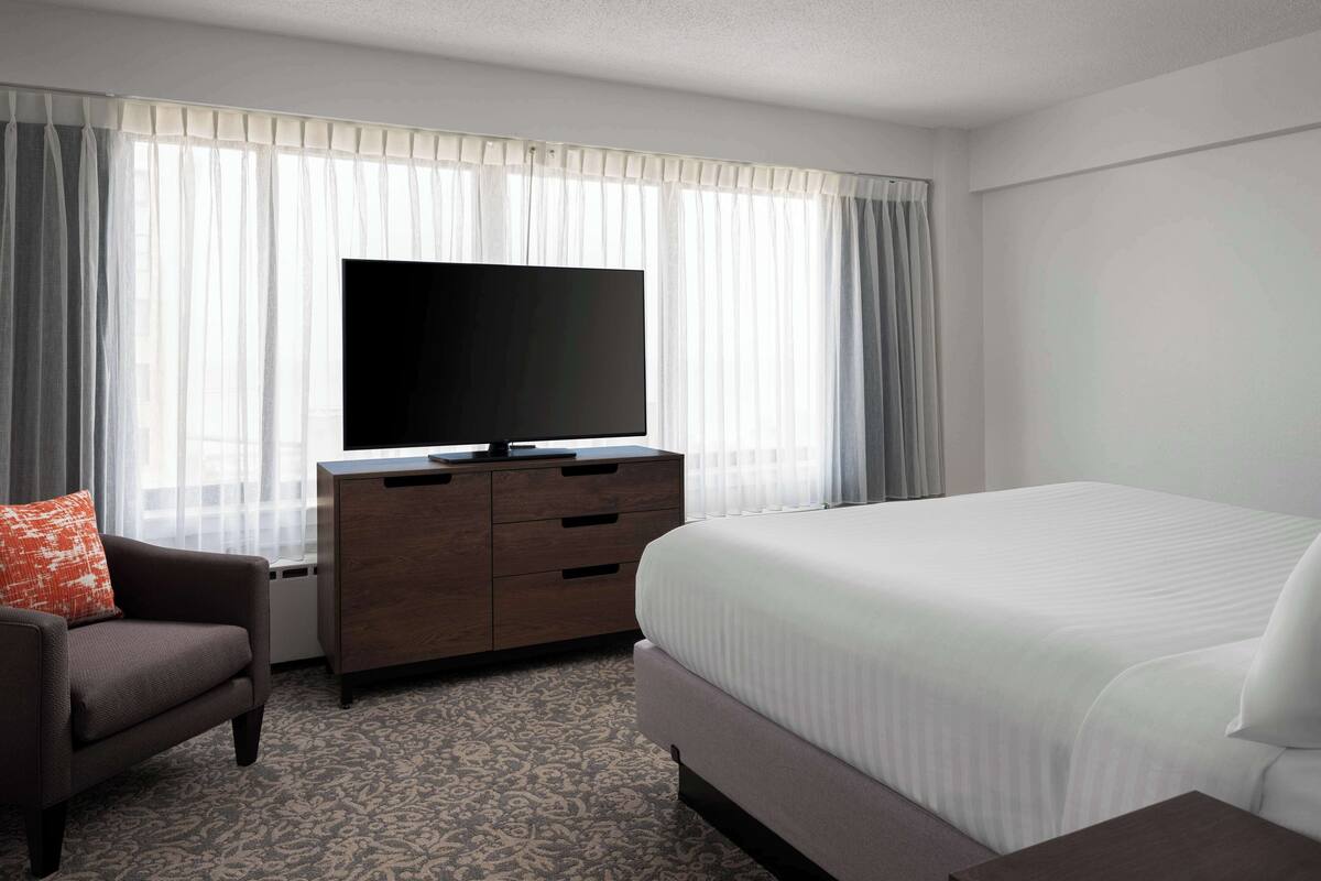 Habitación de hotel con una cama grande, un televisor de pantalla plana, un aparador de madera y una alfombra estampada.