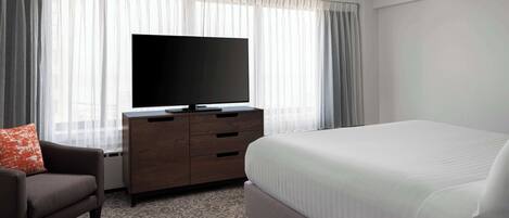 Une chambre d’hôtel avec un grand lit, un téléviseur à écran plat, une commode en bois et une moquette à motifs.