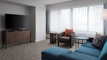 A modern hotel room with a flat-screen TV, a sofa, a chair, and a small table.