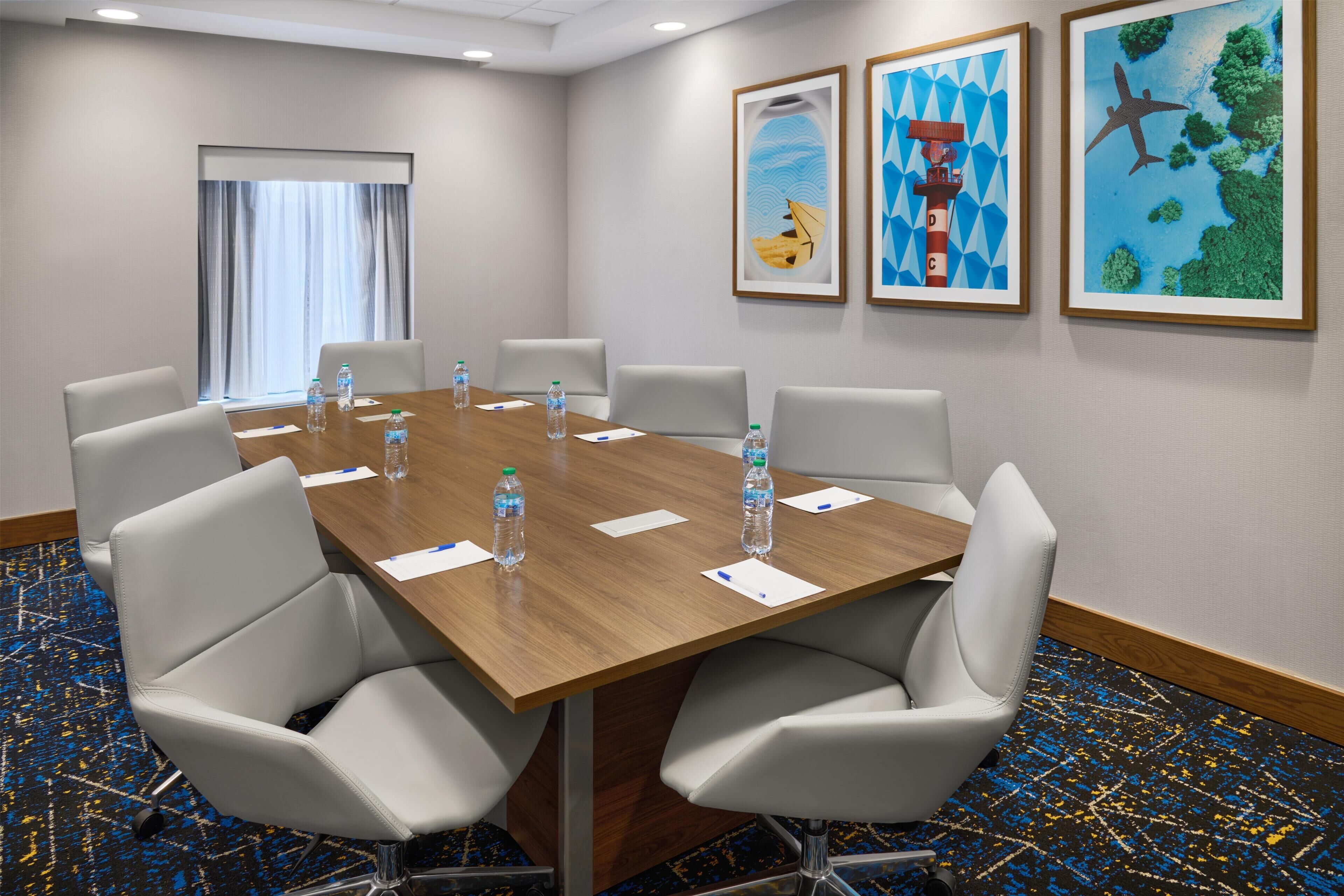 A conference room with a wooden table, white chairs, water bottles, and framed artwork on the walls.