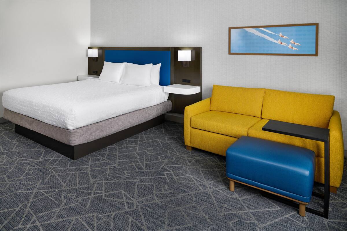 A hotel room with a bed, a sofa, a small table, and a wall-mounted picture.