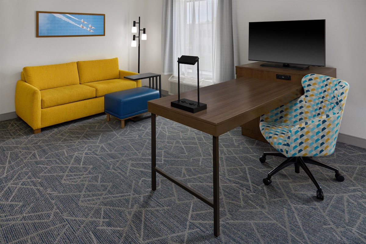 A hotel room with a sofa, a desk, a chair, a TV, and a framed picture on the wall.